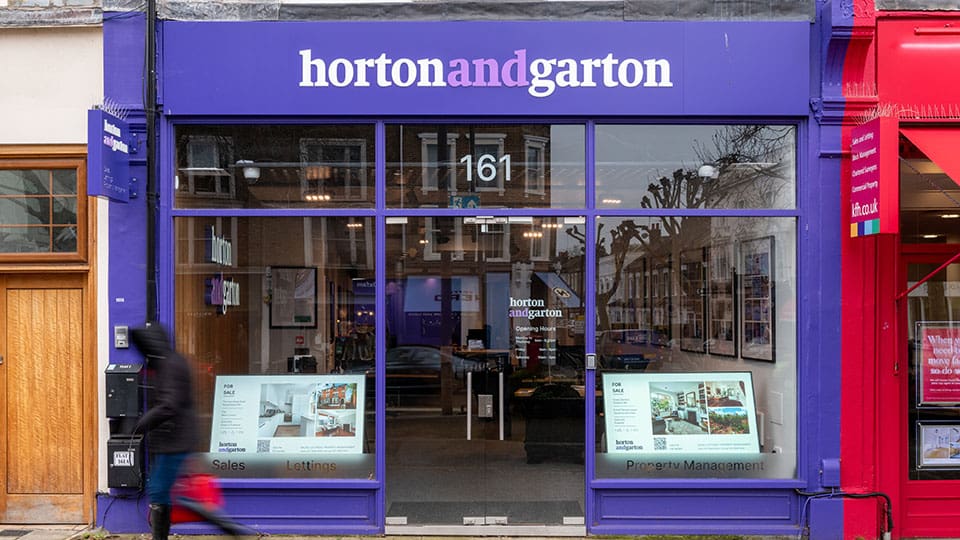 Exterior of Horton & Garton Estate Agents, the building has purple facade with white and purle writing along with clear windows and house adverts in the window
